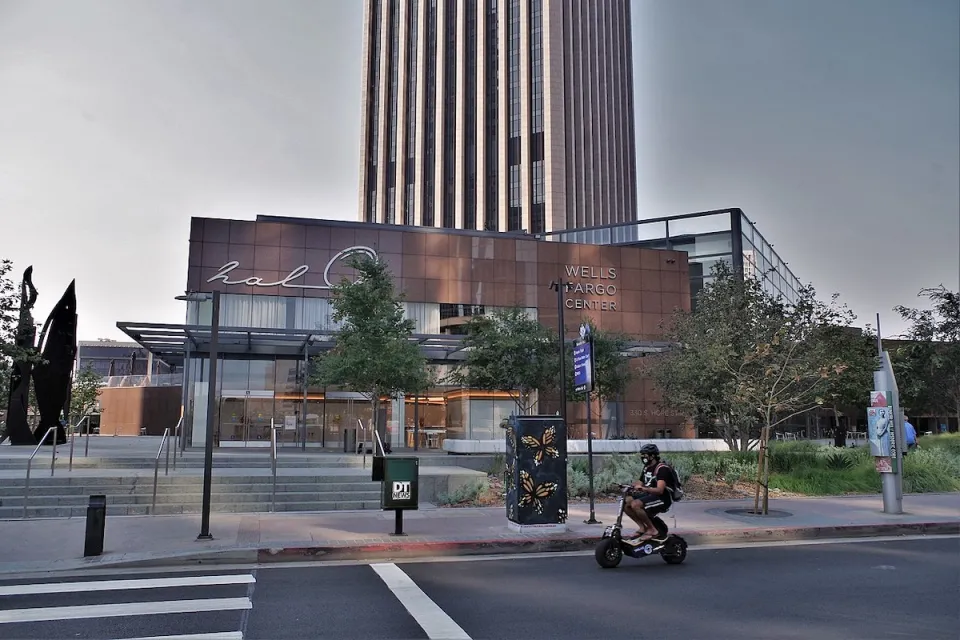 Person on small black e-bike riding on street in front of Wells Fargo Center building in Los Angeles.